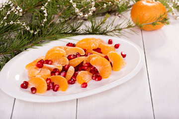 Fresh fruit on a white plate among fur-tree branches. Slices of Mandarin and pomegranate grains. Christmas theme.
