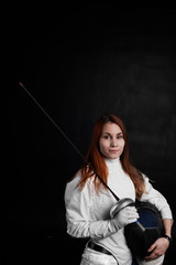 Close-up of woman fencer hends wearing white fencing costume and holding her mask and a sword on black background