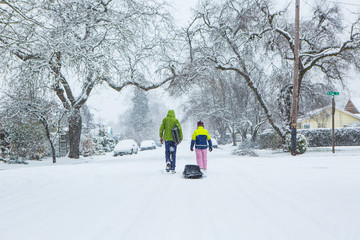 Children walk down the center of an empty street dragging sleds in the freshly fallen winter snow.