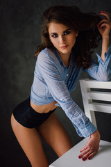 Portrait of sexy young positive woman posing in studio at natural light, wearing blue shirt, has...