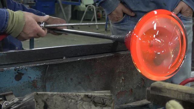 Glassblowing workshop showing glassblower gaffer spinning rod with glowing hot liquid glass vase on work bench using cooling it down then working it with torch amazing colors warm yellow orange 4k