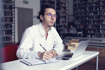 young entrepreneur or university student working on laptop with book on the scientific thesis in a library 