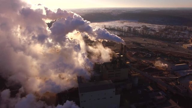 Factory smokestacks steaming and smoking, stunningly illuminated by the cold Winter sunrise, breathtaking aerial view.
