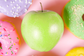 Close-up of tasty donuts and fresh green apple on pink background suggesting healthy food concept