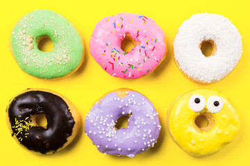 Pink round donut and few other on yellow background. Flat lay, top view.