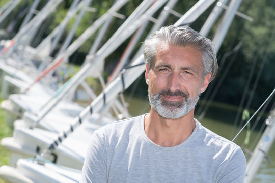 handsome man posing in front of sailing boats and lake