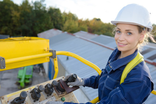 Woman Maneuvering Cherry Picker Above Warehouses