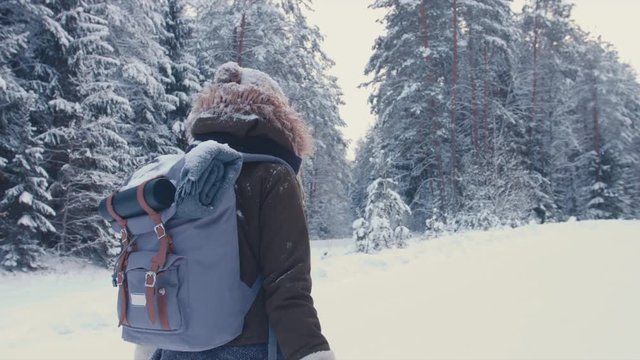 FOLLOW Young female hiking with a backpack in beautiful winter forest, holding paper map in hands. 4K UHD, 60 FPS SLO MO, RAW edited footage