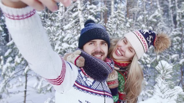 Loving couple wearing bright winter clothes taking photos in snowy forest
