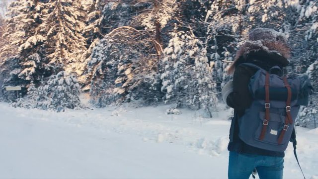 RL PAN Young female hiking with a backpack in beautiful winter forest, walking on a road covered with snow away from the camera. 4K UHD, 60 FPS SLO MO, RAW edited footage