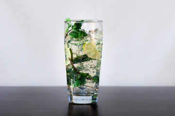 Mojito cocktail with lime, fresh mint and ice in high glass on a black table.
