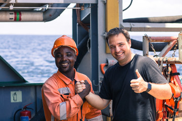 friendship of nations on board of ship/vessel. African seaman and European Chief Mate smiling and shaking hands on deck. - obrazy, fototapety, plakaty