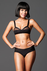 Smiling stylish woman in black underwear with a slim  body is standing on a gray background