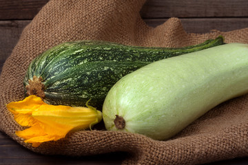 green zucchini and courgette with a flower on sackcloth wooden background