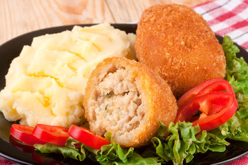 three fried breaded cutlet with mashed potatoes lettuce on a black plate and wooden background