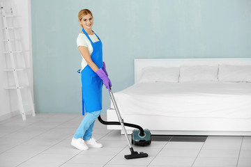 Fototapeta na wymiar Pretty adult woman hoovering floor with vacuum cleaner