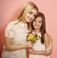 Beautiful young woman and her daughter with bouquet of flowers on color background. Mother's day concept