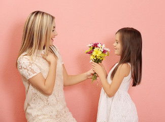 Little girl giving bouquet of flowers to her mother, on color background. Mother's day concept