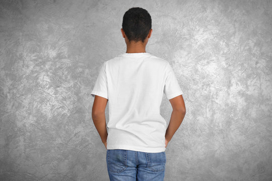 Young African American boy in blank white t-shirt standing against textured wall