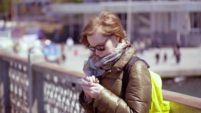 SLOW MOTION: young woman looks at her smartphone. Cute red hair girl looks for the information in her smartphone and then smiles to the camera.
