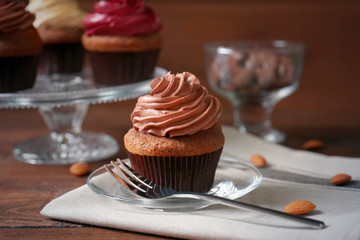Plate with tasty cupcake, fork and napkin on wooden table