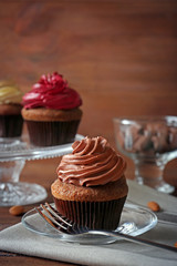 Plate with tasty cupcake, fork and napkin on wooden table