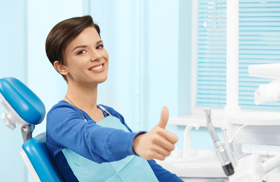 Young Female Patient Visiting Dentist Office.Beautiful Smiling Woman With Healthy Straight White Teeth Sitting At Dental Chair And Making Thumbs Up.Dental Clinic.Stomatology