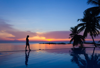 Woman silhouette walking over infinity pool at sunset in Koh Phangan, Thailand