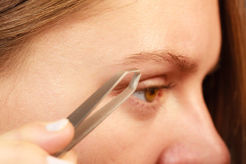 Woman tweezing eyebrows depilating with tweezers