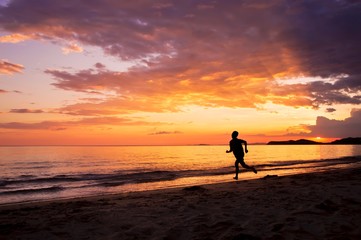 Silhouette of happy man running on the beach at sunset