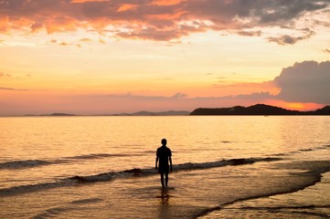 Silhouette of lonely man walking in to the sea at sunset