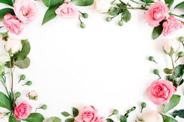 Round frame made of pink and beige roses, green leaves, branches on white background. Flat lay, top...