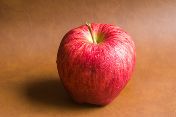 red apple with drop of water on skin put on brown background. Healthy fruit