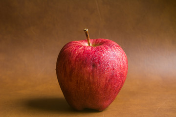 red apple with drop of water on skin put on brown background. Healthy fruit