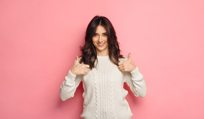 brunette woman showing thumbs up and smiling over pink background