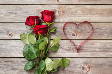 bouquet of red roses on wood background with heart from ribbon.