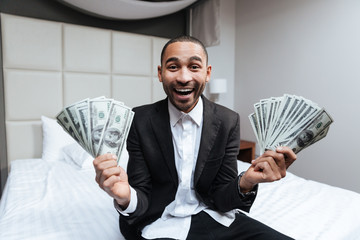 Happy African man with money on bed