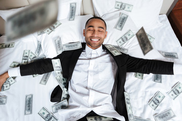 African man lying on bed with falling money