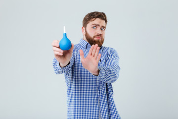 Worried bearded young man holding and rejecting of enema