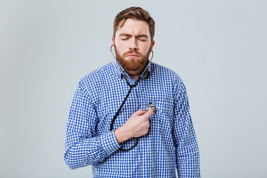 Concentrated man with closed eyes using stethoscope and feeling heartbeat