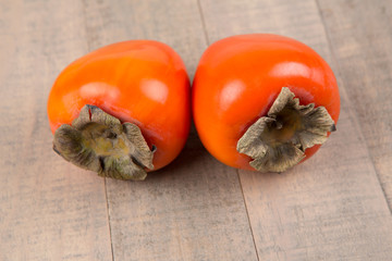 Two whole persimmmons isolated on a wood background
