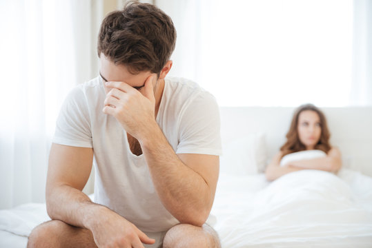 Depressed man sitting on bed and having problems with girlfriend
