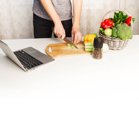 Man preparing a salad, searching for recipes on-line using a laptop hands close up, kitchen tools and food ingredients 