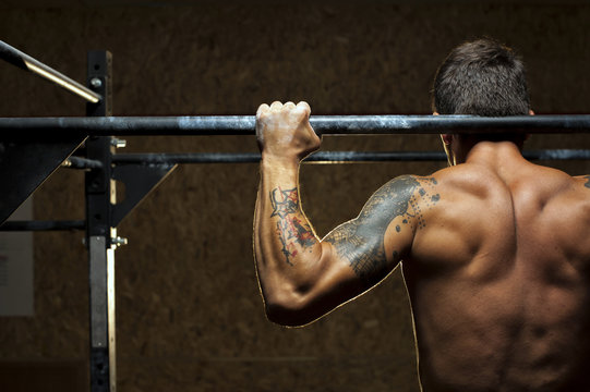 Muscular man doing pull up exercise on bar in gym
