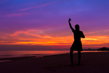 Silhouette of woman with hands up while standing on sea beach at