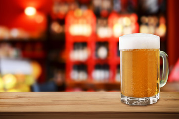Mug of cold beer with foam on wooden table in pub