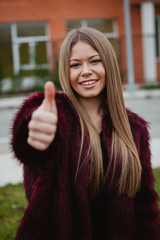 Stylish girl with long hair and fur coat saying Ok