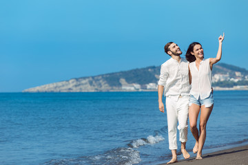 Couple walking on beach. Young happy interracial couple walking on beach smiling holding around each other.