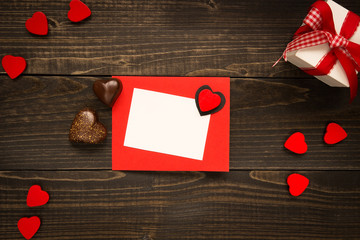 Valentine's Day card on the wooden background. Gift box, red hearts and chocolate on the wooden desk.