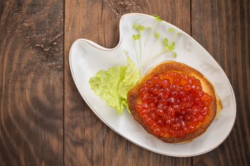 healthy appetizer : sandwich with red caviar on white china plate. Wooden background. Top view. Close-up
